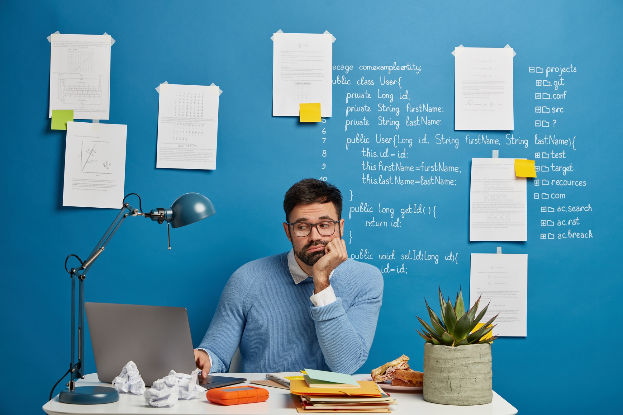 Concentrated bearded web developer improves new website version, sits at white table, loaded with no